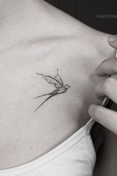 a woman's chest with a small hummingbird tattoo on her left side ribcage