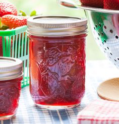 jars filled with jam sitting on top of a table next to baskets of strawberries