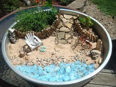 an outdoor garden with rocks, gravel and plants in a metal bowl on a wooden table