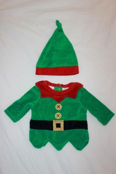 a green and red christmas outfit laying on top of a white bed next to a stuffed animal