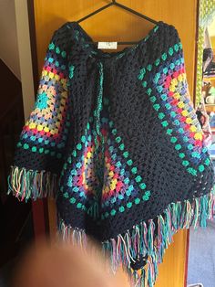 a colorful crocheted sweater hanging on a wooden hanger in front of a door