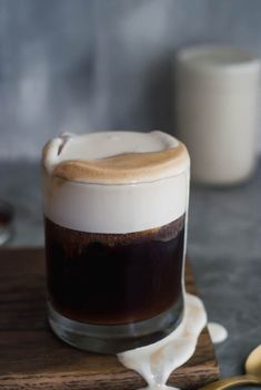 a glass filled with liquid sitting on top of a wooden table next to a spoon