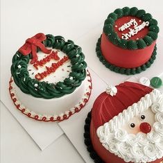 three decorated cakes sitting on top of a white table next to each other and one has a santa claus face