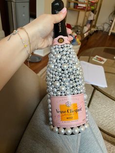 a woman holding a bottle of wine with pearls on the bottom and an arm around it