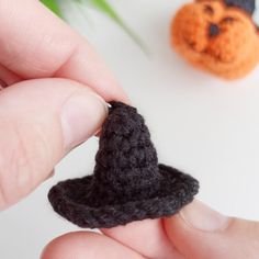 a hand holding a tiny black hat next to a small orange pumpkin ornament