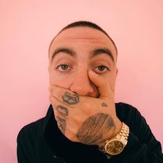 a man covering his mouth with both hands and looking at the camera while standing against a pink wall