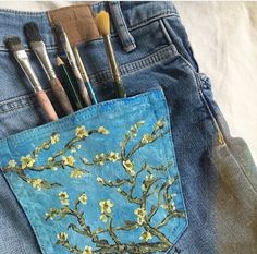 a pair of jeans with paintbrushes in the pocket and an image of a blossoming tree painted on it