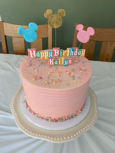 a pink birthday cake with mickey mouse toppers and sparkles on it, sitting on a table