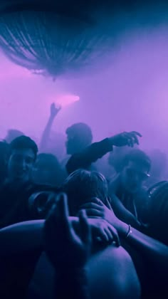 a group of people standing around each other in front of a purple light with their arms up