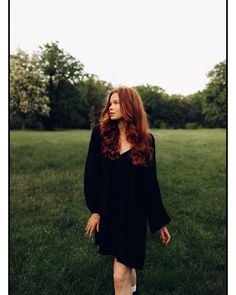 a woman with long red hair standing in the grass