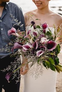 a bride and groom standing next to each other on the beach with flowers in their bouquet