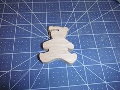 a wooden keychain shaped like a teddy bear on a cutting board with scissors