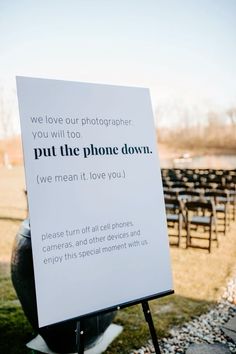 a sign that is sitting in the grass near some chairs and an empty field behind it