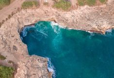 an aerial view of the ocean with rocks and blue water in the foreground, from above