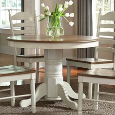 a white table with two chairs and a vase filled with tulips on top