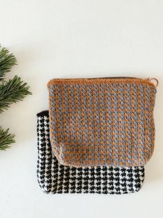 two purses sitting next to each other on top of a white table with pine branches