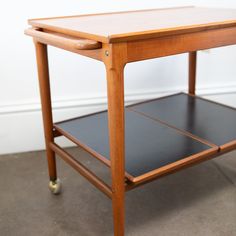 a wooden table sitting on top of a floor next to a white wall with a black shelf underneath it