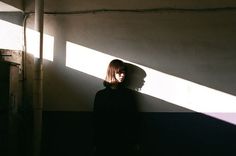 a woman standing in front of a wall with the sun shining on her face and hair