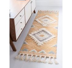 a beige rug with tassels on the floor in front of a white dresser