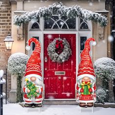 two garden gnomes are standing in front of a red door with wreath and wreath on it