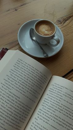 an open book sitting on top of a wooden table next to a cup of coffee