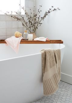 a white bath tub sitting under a window next to a vase with flowers in it