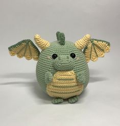 a crocheted green dragon sitting on top of a white surface with snow falling around it