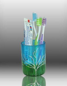 three toothbrushes in a cup on a reflective surface