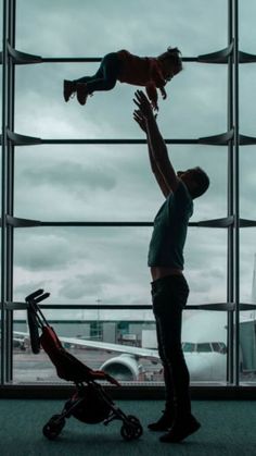 a man holding a baby in his arms while standing next to an airport terminal window