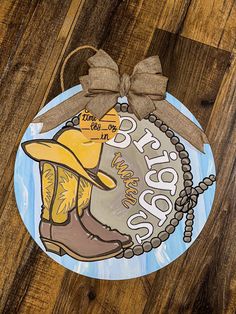 a painted cowboy boot ornament hanging on a wooden floor with a brown bow