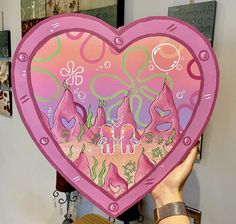 a woman holding up a pink heart shaped painting