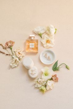 an arrangement of flowers and personal care items on a white surface with a bottle of perfume in the middle