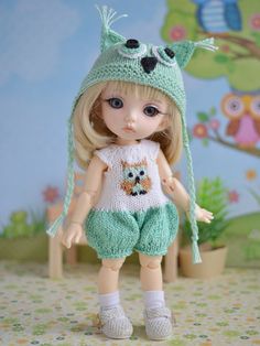 a doll wearing a knitted hat and green pants with an owl on it's chest