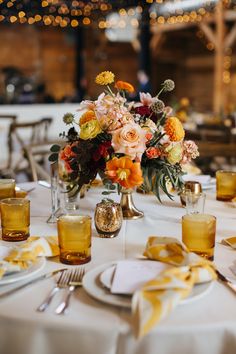 an arrangement of flowers and candles on a table with napkins, silverware and glasses