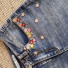 a pair of jeans with embroidered flowers on the back pocket and side pockets, sitting on a piece of fabric