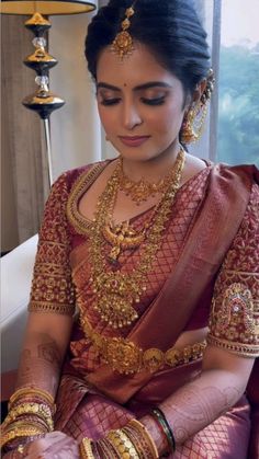 a woman in a red and gold sari sitting on a couch with her hands together