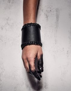 a person wearing a black leather bracelet with chains on their wrists and hand in the air