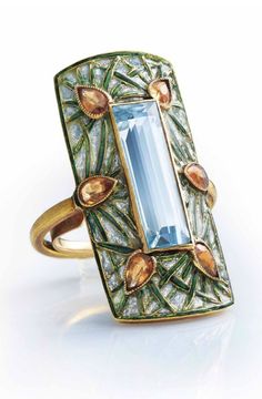 GEORGES FOUQUET - AN ART NOUVEAU AQUAMARINE, GARNET AND ENAMEL RING, CIRCA 1900. Set with a rectangular-cut aquamarine within a rectangular bombé panel of green and blue window enamel of stylised pine design, applied with six pear-shaped spessartite garnets, with French assay mark for gold, signed G. Fouquet, numbered, with maker's marks for Georges Fouquet. Georges Fouquet, Blue Window, Art Nouveau Ring, Aubrey Beardsley, Nouveau Jewelry, Pine Design, Jewelry Brands, Art Nouveau Jewelry