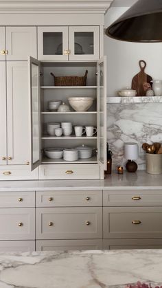 a kitchen with marble counter tops and white cabinets, gold pulls on the cupboards