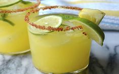 two glasses filled with lemonade and limes on top of a marble countertop