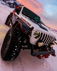 a white jeep driving down a snow covered slope at sunset with the sun setting in the background