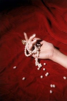 a woman's hand with beads on it laying on a red sheet and holding onto her fingers