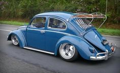 a blue vw bug is driving down the road with its roof rack on it's back end