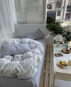 a bed sitting next to a window in a room with white curtains and pillows on it