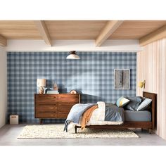 a bed room with a neatly made bed next to a wooden dresser and lamp on the wall