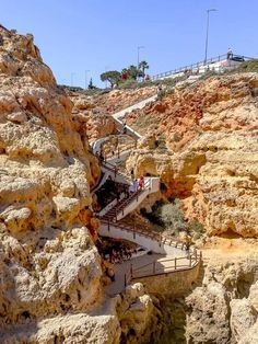 stairs leading up to the top of a rocky cliff with people walking down them and onlookers in the distance