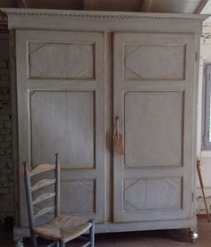 an old white armoire sitting in a room next to a wooden chair and window