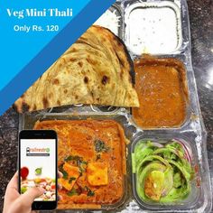 a person holding a cell phone in front of a tray of food with different types of vegetables