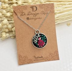 a necklace with a flower on it sitting next to a card and some dried flowers