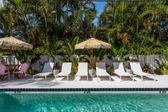 lounge chairs and umbrellas next to a swimming pool with palm trees in the background